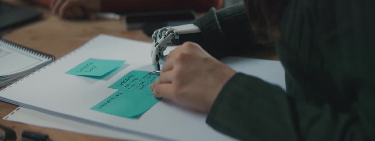 A woman with a prosthetic mechanical hand reading post its from a large paper pad