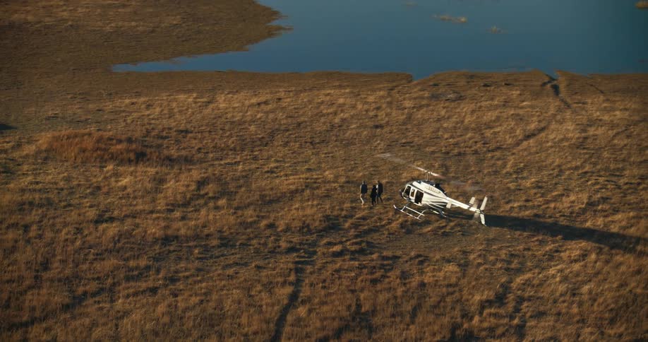 Top view of a helicopter landing in a jungle by a lake and people walking