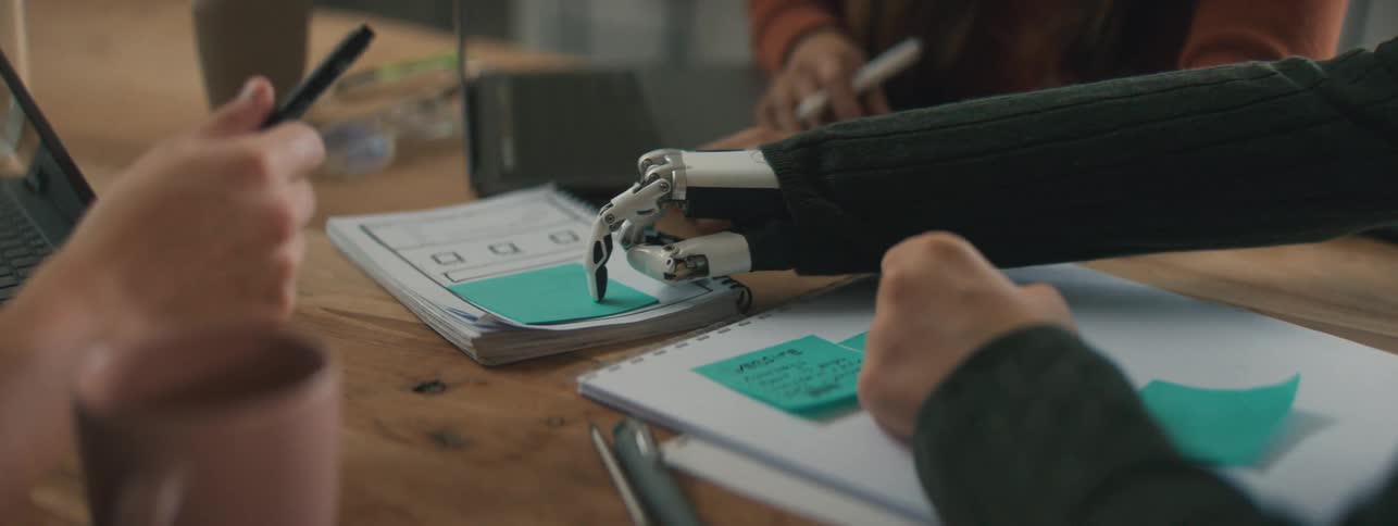 Three people stick tags on notebooks while sitting at a table together