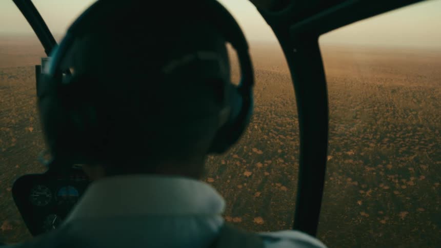 The back of a helicopter pilot flying over a rural area with lots of vegetation