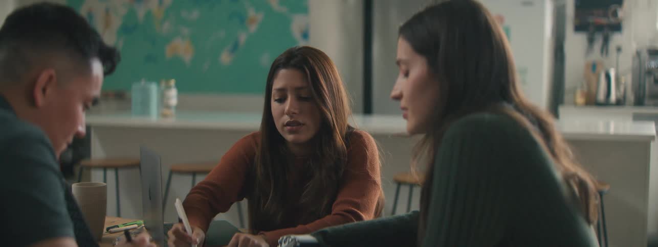 Three people engaged in a collaborative work session at a table with a map visible on the wall behind them