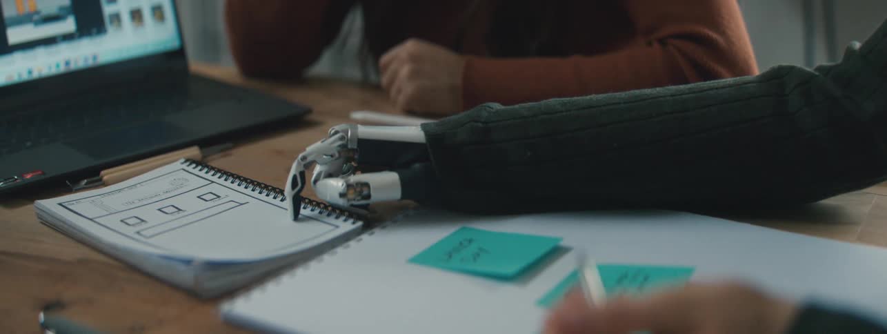A robotic hand points to a paper and then a human hand writes on another paper