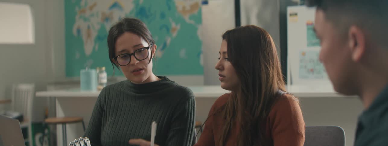 Two women and a man are gathered around a table and are talking while studying