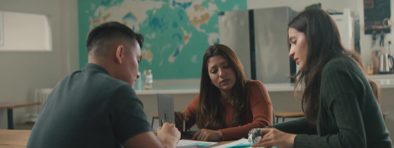 Two women and a man are sitting around a table and looking at a paper that is in the center of the table