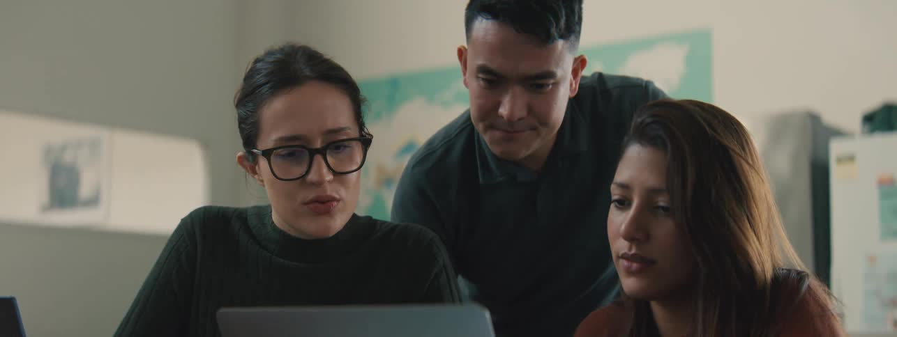 Two women sitting and a man standing behind all interacting with a laptop in front