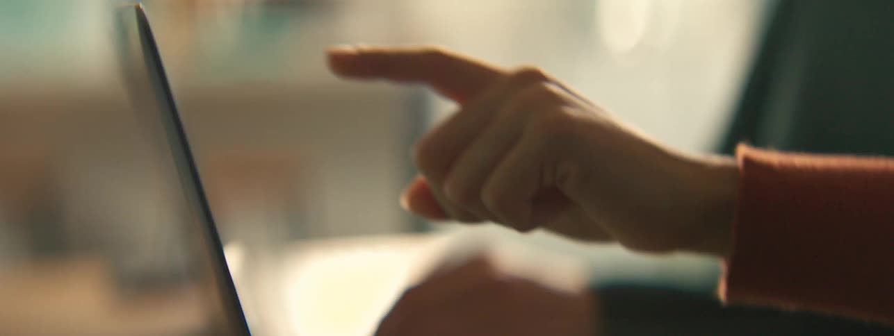 The finger of a person wearing an orange sleeveless outfit pointing at a laptop screen