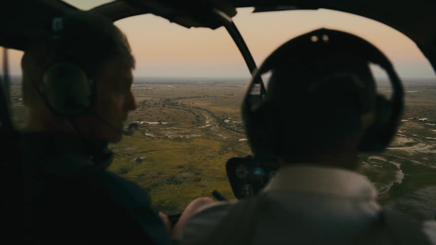 Inside view of a helicopter with two pilots flying over a jungle area