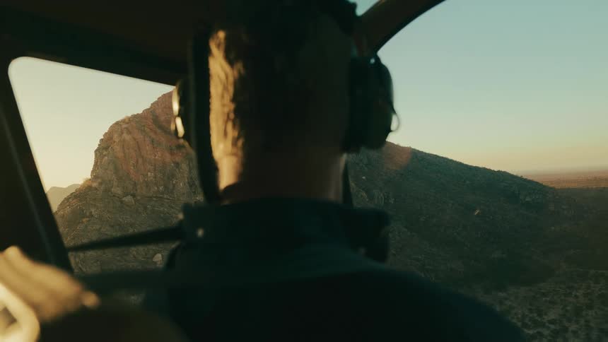 View from inside a helicopter with a pilot looking at a mountainous landscape during sunset
