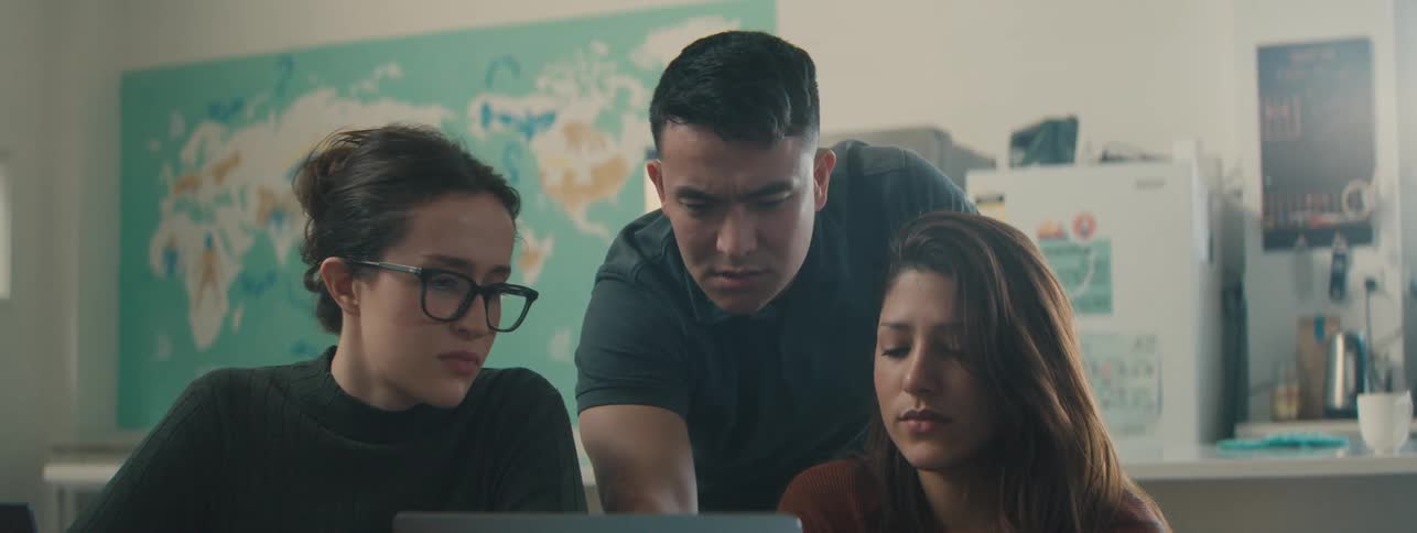 Two women and a man are talking while looking at a laptop screen in a classroom