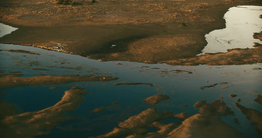 A helicopter flying over a river that is partially dry in the savanna