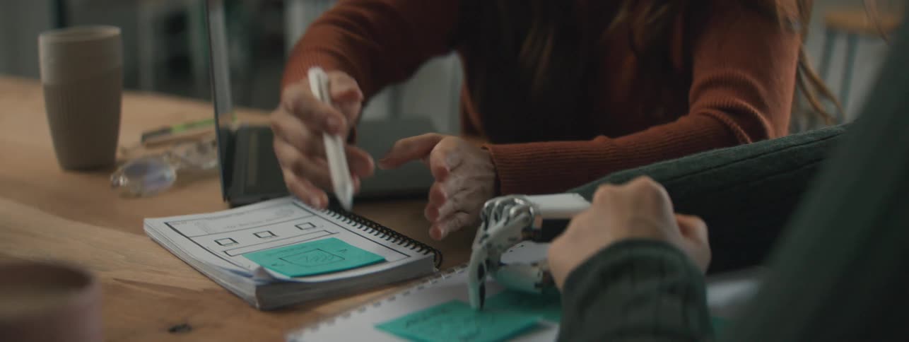 Hands of three people at a table writing in a notebook and discussing