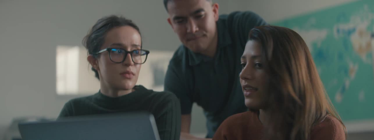 In an office setting three people are engaged in a discussion about something on a laptop screen