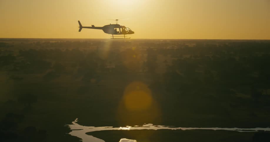 Helicopter flying above a forest with the river and an orange sky with the sun on the horizon
