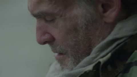 A bearded homeless man sits on the ground