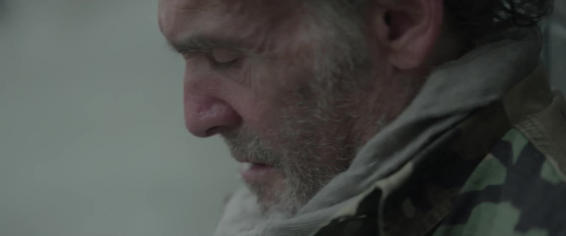 A bearded homeless man sits on the ground