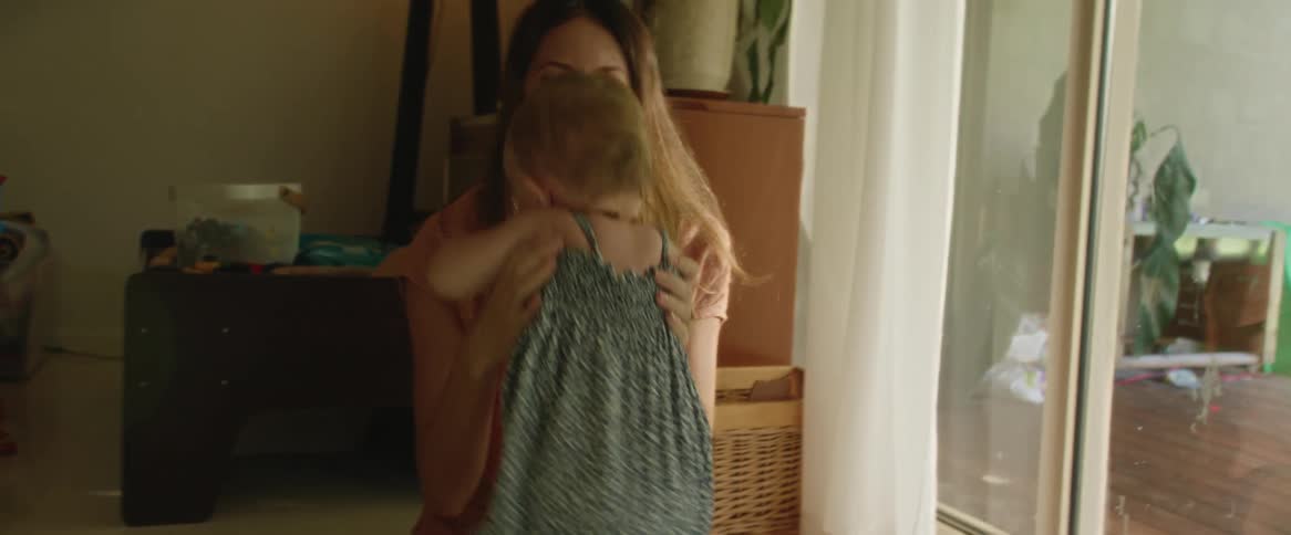 A baby walks up to her mother who is sitting and they both smile