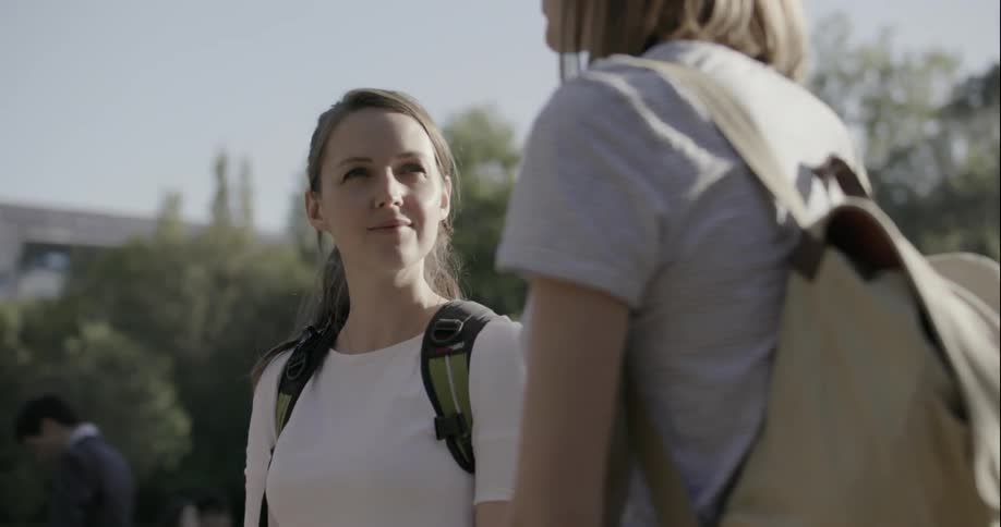 Two women standing outside wearing backpacks and talking