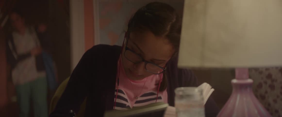 A girl studying at a desk as her mother approaches behind her
