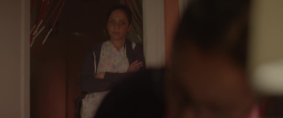 A young girl is doing her homework while her mother watches from the doorway