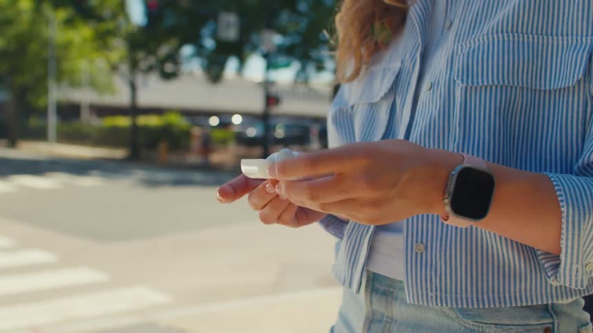 A person is removing wireless earbuds from their case while standing at a crosswalk