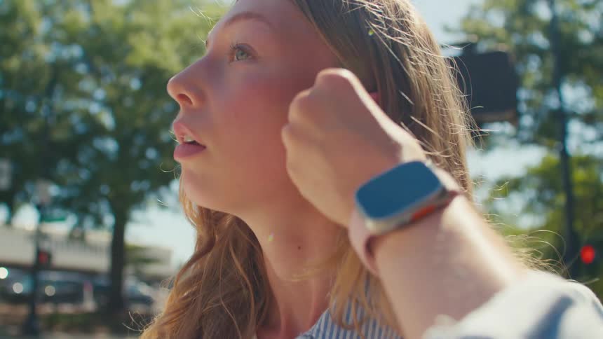 Woman standing near a busy street on a sunny day inserts an earbud
