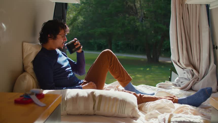 A man enjoys a hot beverage on a bed inside a modern tent