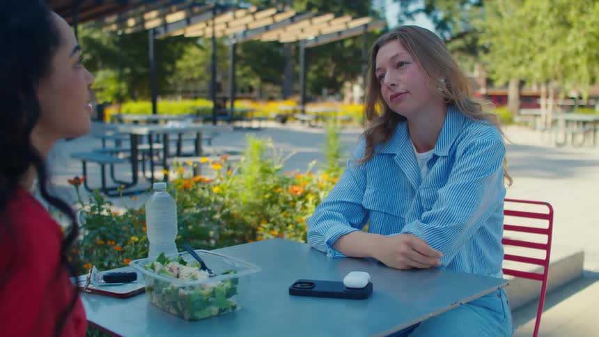 Female friends talks while eating lunch at an outdoor table in the park