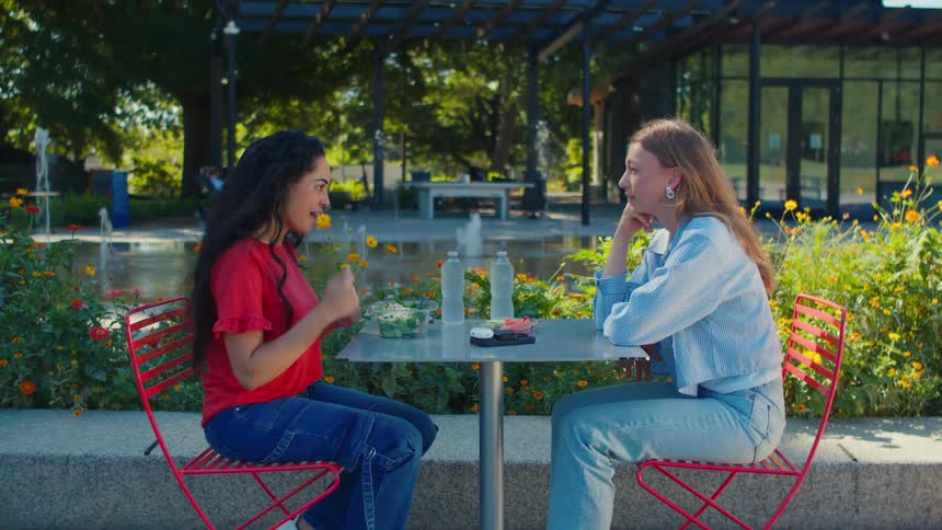 Two friends seated at an outdoor table beside a bubbling fountain engaged in conversation