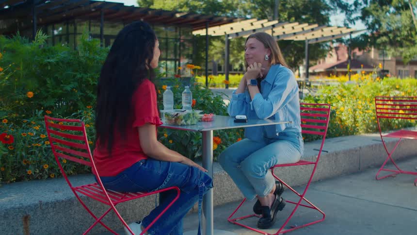 Two women sitting at a table in an outdoor setting talking and having bottles of water and salad
