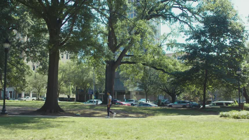 A person walking on a grassy path in a park surrounded by tall trees