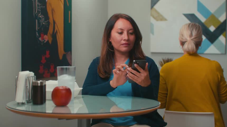 A woman sitting in a restaurant picks up her smartphone and dials