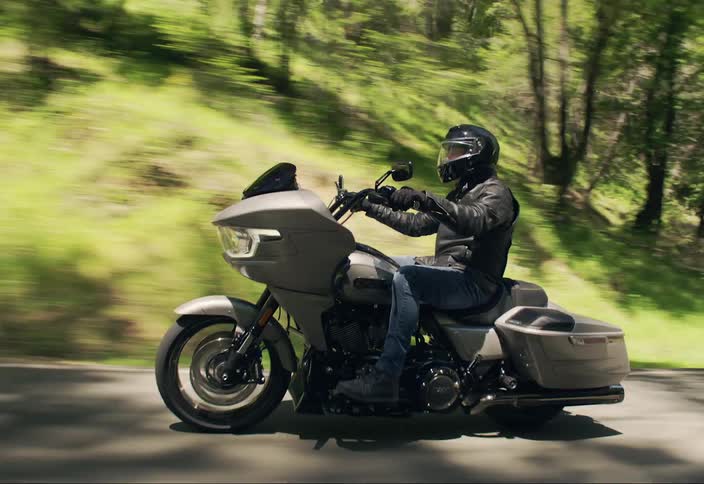 A man driving a motorcycle on a road near a forest
