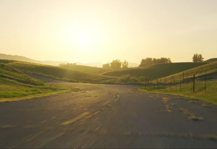 The sun shines over grassy hills and forests