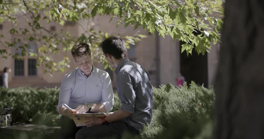Two men sit on a bench browsing a book