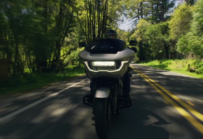 Person riding a modern motorcycle on a paved street during the day and surrounded by vegetation
