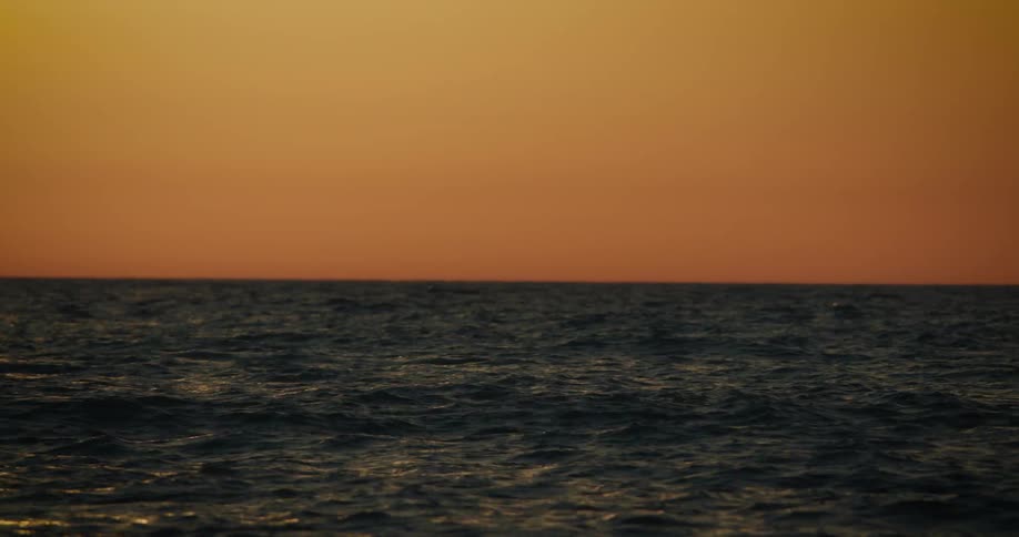 A dark choppy sea beneath a vibrant orange sunset