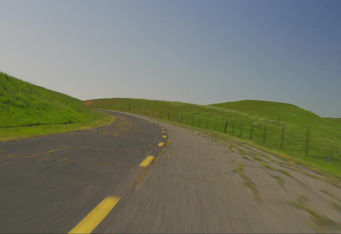 Moving point of view on a paved road surrounded by hills during the day