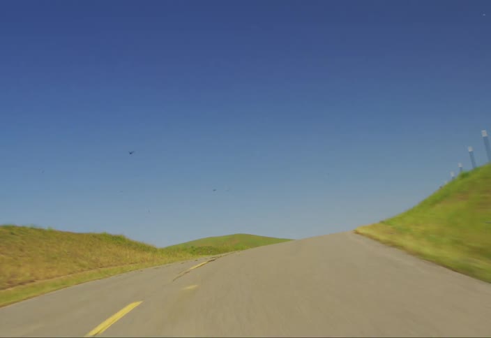 Moving point of view of a narrow highway in the middle of rural fields and hills