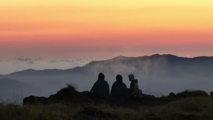Three people silhouetted against a vibrant sunset overlooking a vast landscape