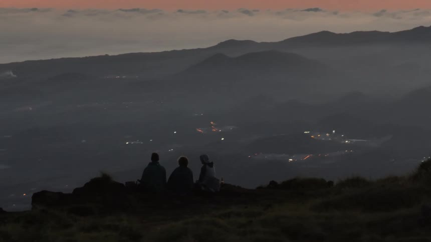 Three adventurers sitting on a mountain cliff overlooking a cityscape in a sea of clouds with a reddish sky