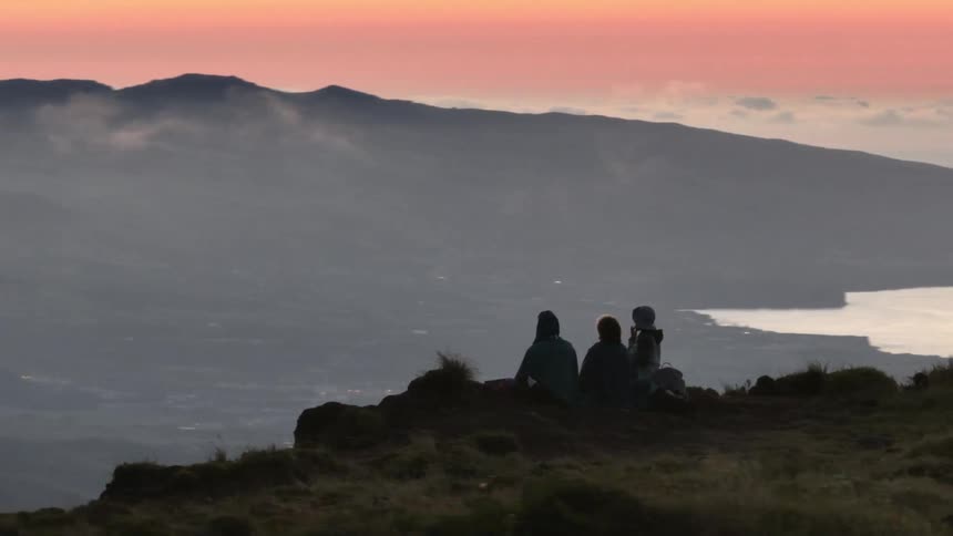 Three people silhouetted against a vibrant sunset overlooking a vast landscape