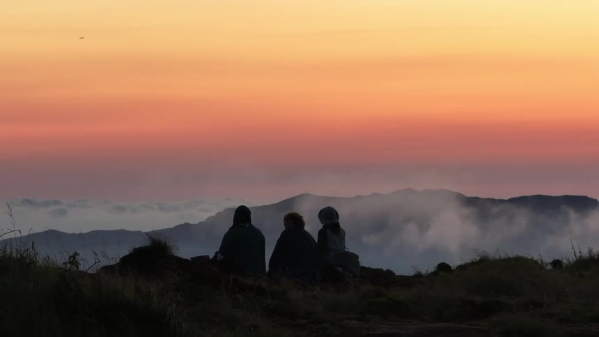 Three people silhouetted against a vibrant sunset overlooking a vast landscape