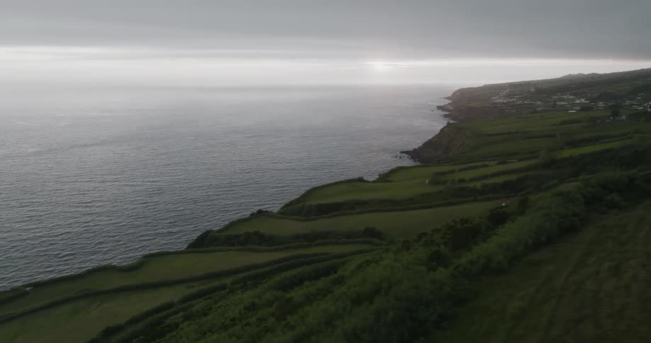 Aerial view of a coastline stretching into the distance with lush green fields at sunset