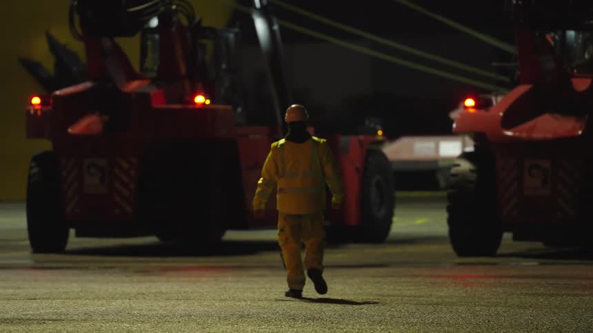 Worker in an uniform walks across a parking lot toward a heavy commercial vehicle at night