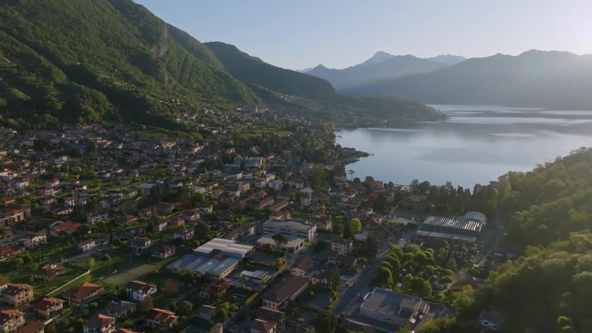 An aerial view of a city facing a lake between mountains and with many trees around