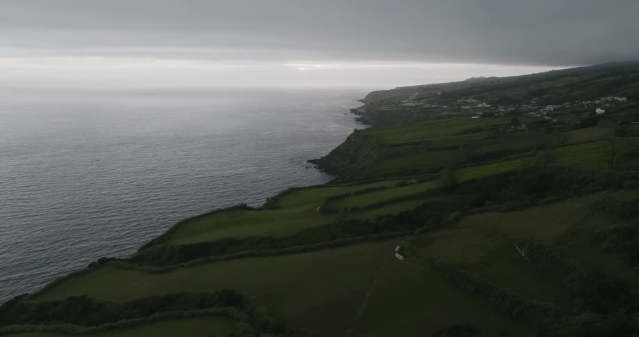 Fields slope toward the water near a coastal town on an overcast day