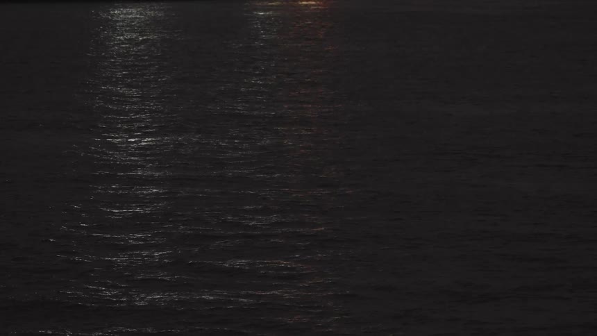 Reflection of light on a calm moving sea at night