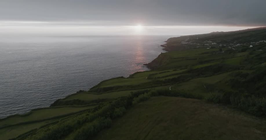 Aerial view of a coastline stretching into the distance with lush green fields at sunset