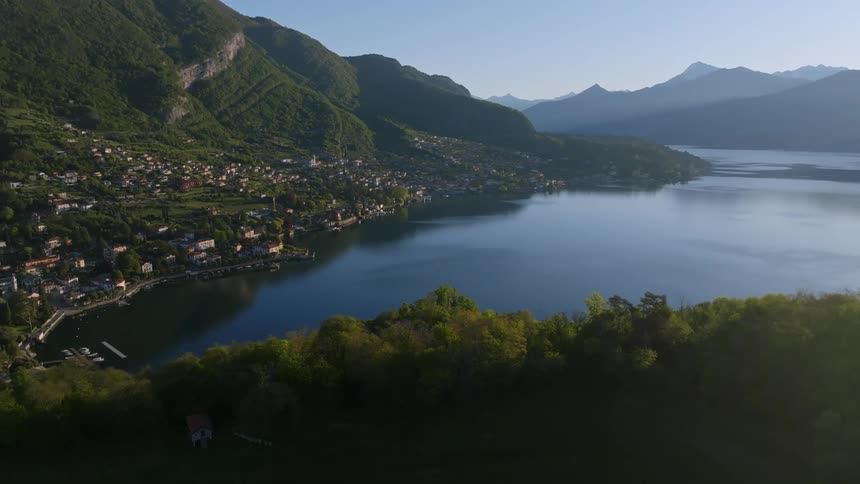 An aerial view of a lakeside town nestled on the mountainside next to a clear lake reflecting the sky