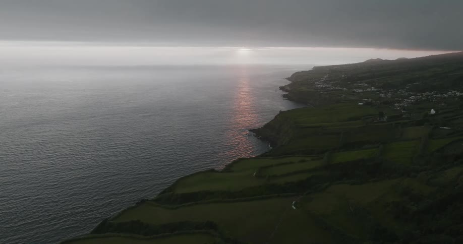 Low lying clouds temporarily obscure the sun setting over the ocean near a coastal town